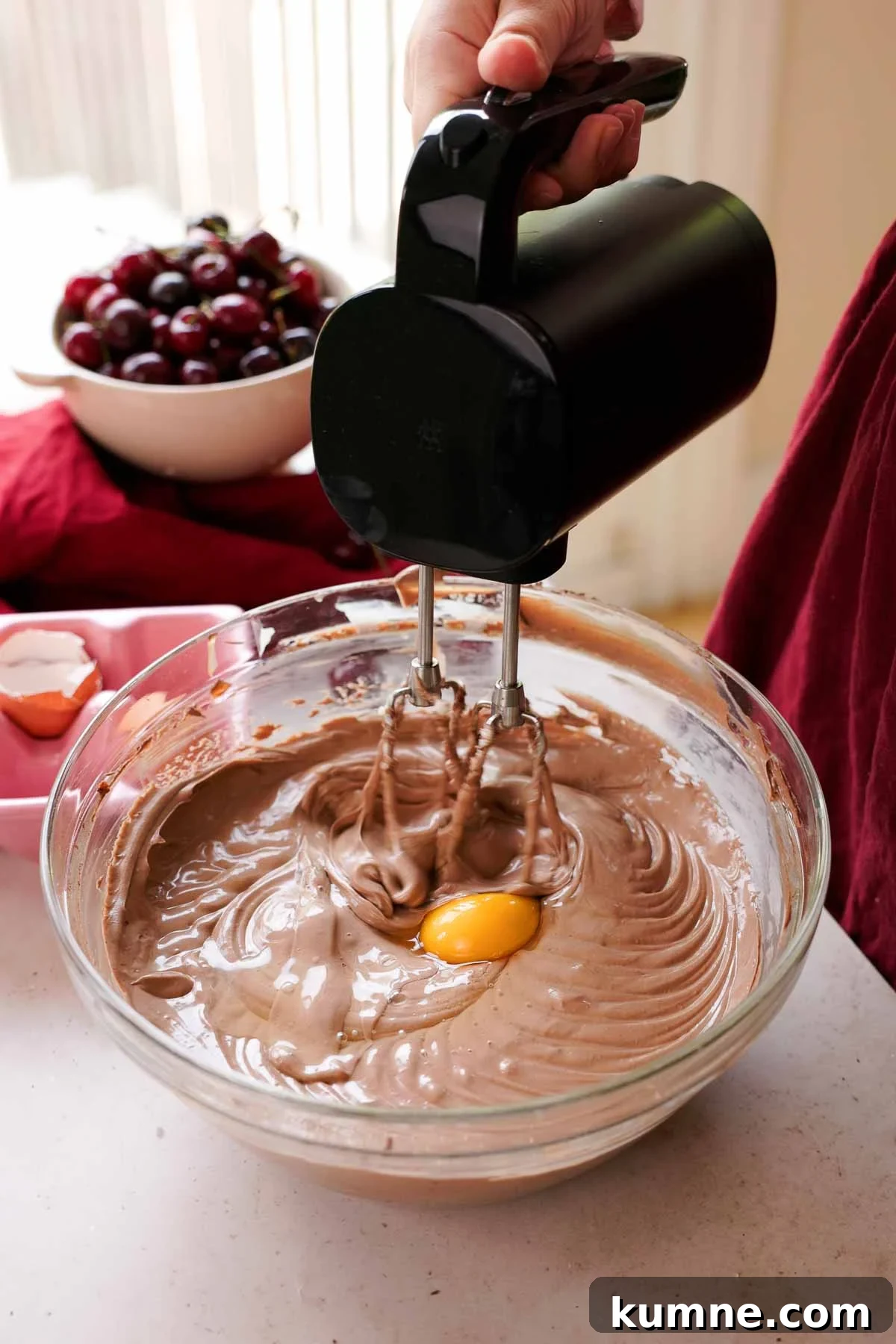 adding eggs into chocolate cheesecake batter one by one