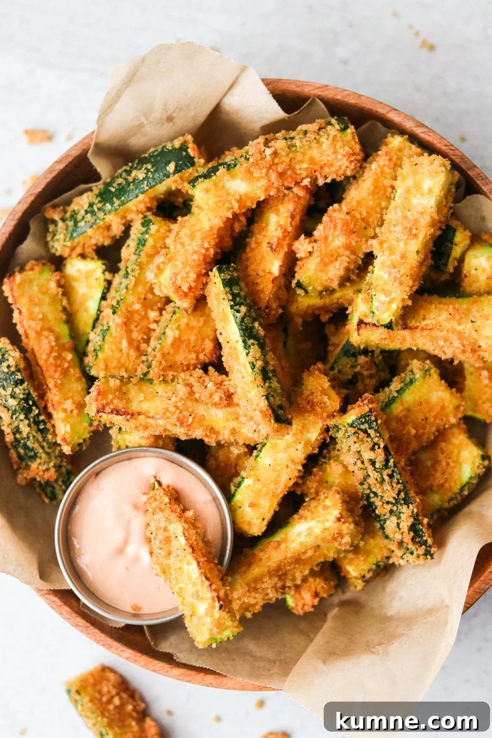 Keto Air Fryer Zucchini Fries Recipe for Low-Carb Snacks 5 an overhead shot of air fryer zucchini fries in a brown bowl with one dipping into a sauce.
