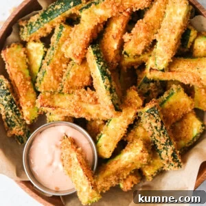 Keto Air Fryer Zucchini Fries Recipe for Low-Carb Snacks 7 an overhead shot of air fryer zucchini fries in a brown bowl with one dipping into a sauce.