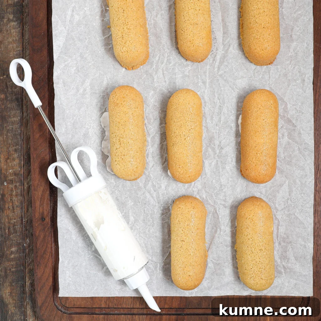 Eight golden ladyfinger cookies are arranged on parchment paper over a wooden surface with a piping tool beside them.