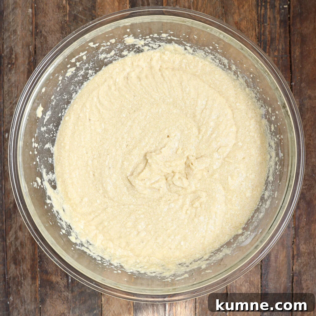A glass mixing bowl filled with pale, creamy batter for homemade Twinkies sits on a rustic wooden surface.