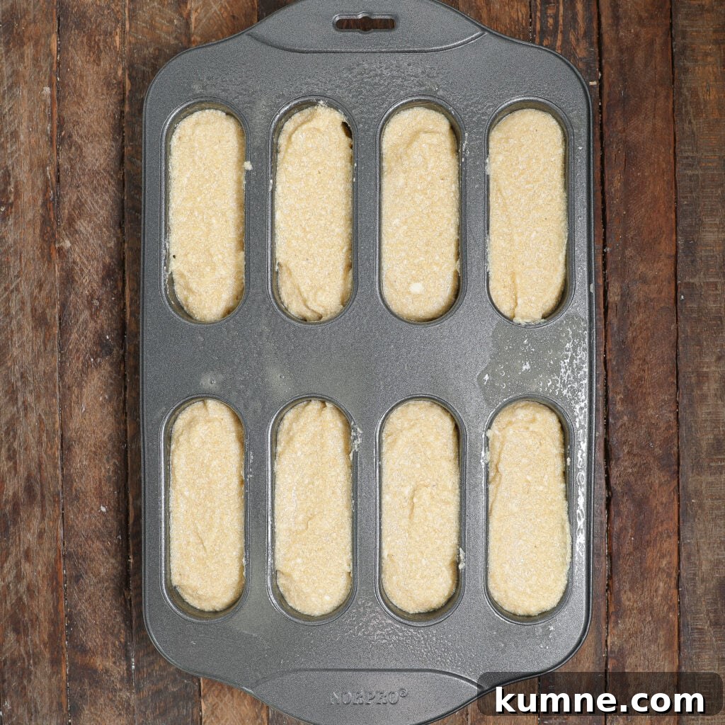 A metal baking pan with eight oval molds, perfect for homemade Twinkies, is filled with batter and ready to be baked.
