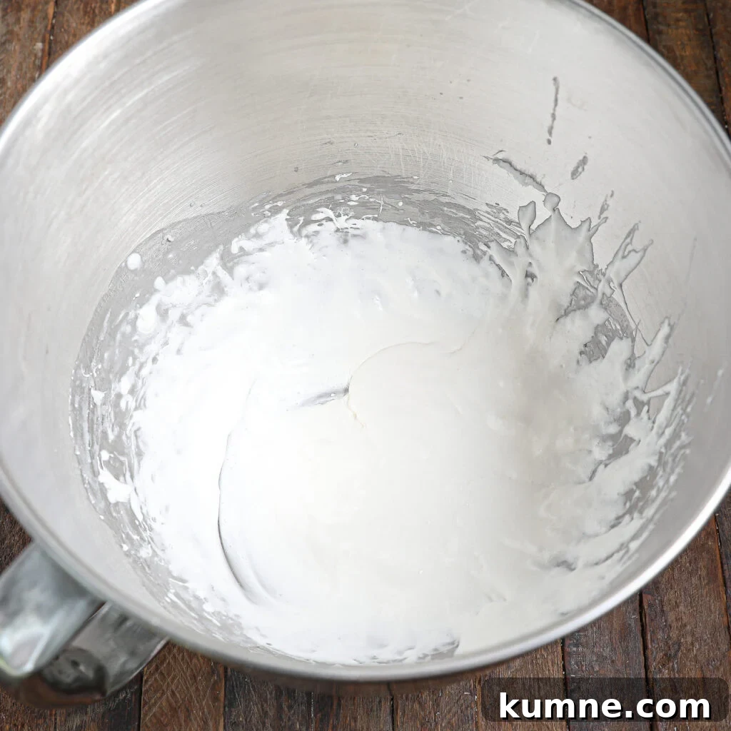 A stainless steel mixing bowl containing partially mixed white icing or frosting for homemade Twinkies, set on a wooden surface.