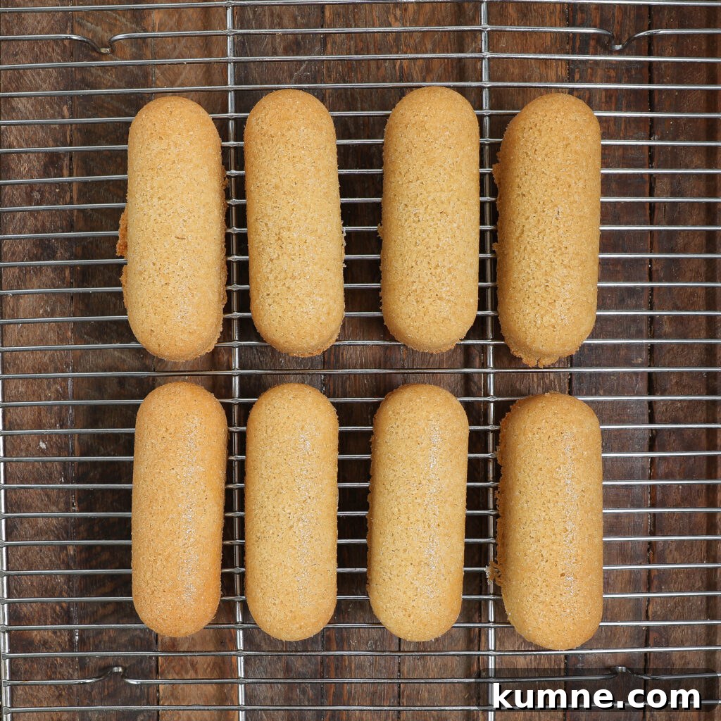 Eight golden brown homemade Twinkies are neatly arranged in two rows on a metal cooling rack.
