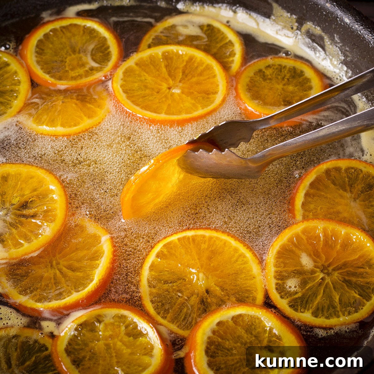 Using metal tongs to turn orange slices in simmering simple syrup.