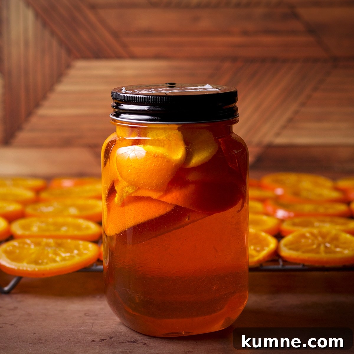 A jar of orange-infused simple syrup in front of a wire rack with candied orange slices drying.
