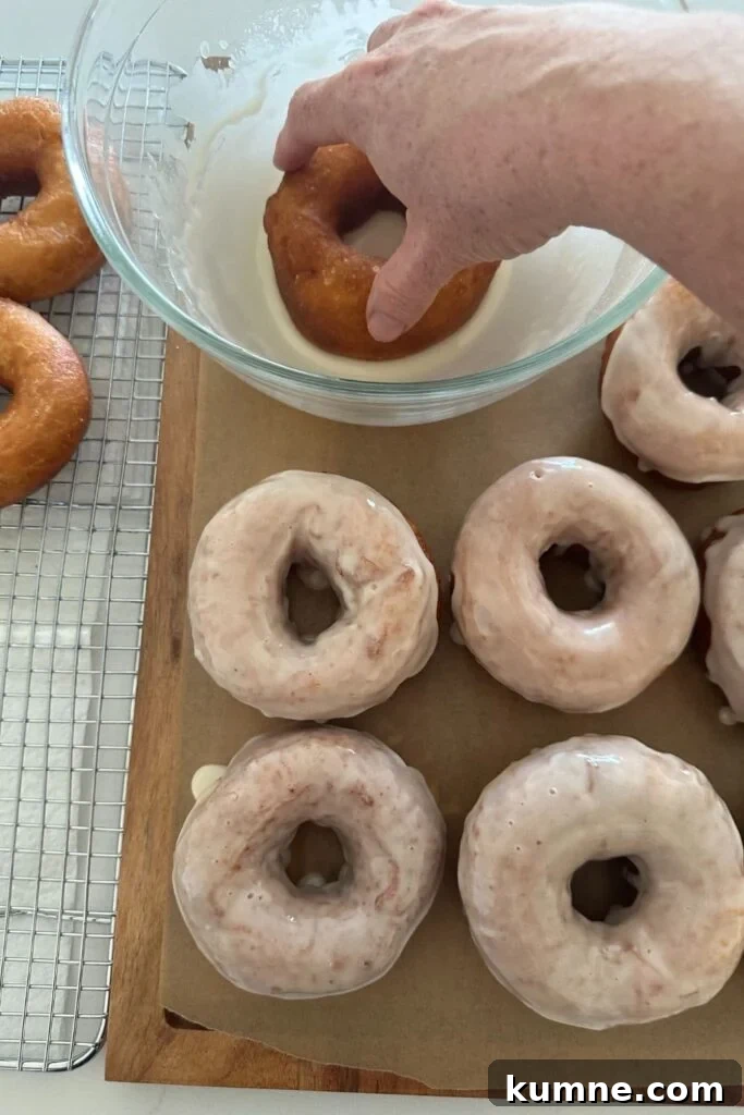 Dipping fried sourdough donuts in a vanilla glaze.