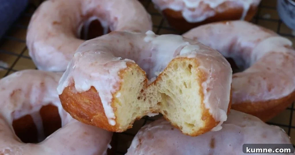 Fried sourdough donuts coated in vanilla glaze. There is a bite taken out of the donut so you can see the light, airy interior.