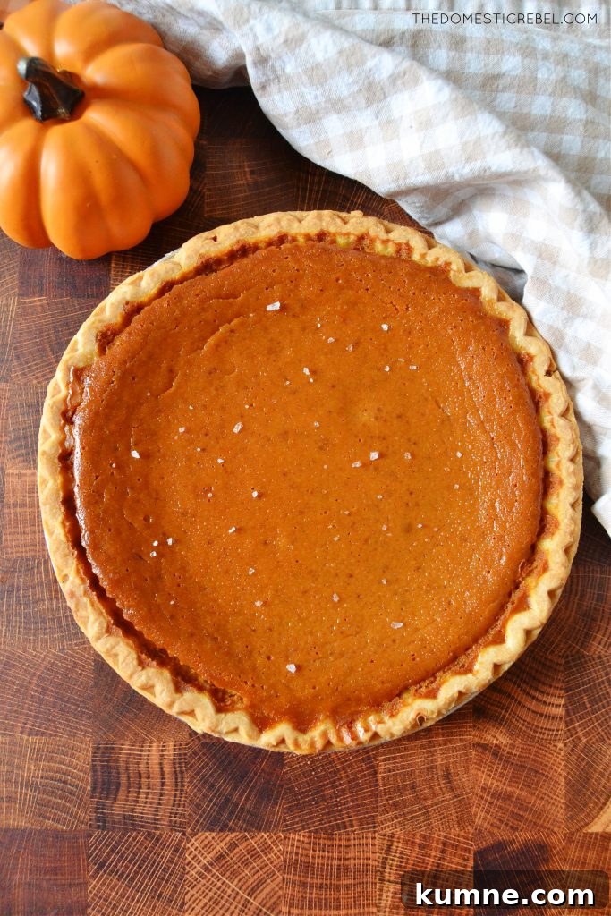 Salted Caramel Pumpkin Pie Recipe for Fall Desserts 4 a whole salted caramel pumpkin pie on a wood board next to a dishtowel and a mini pumpkin