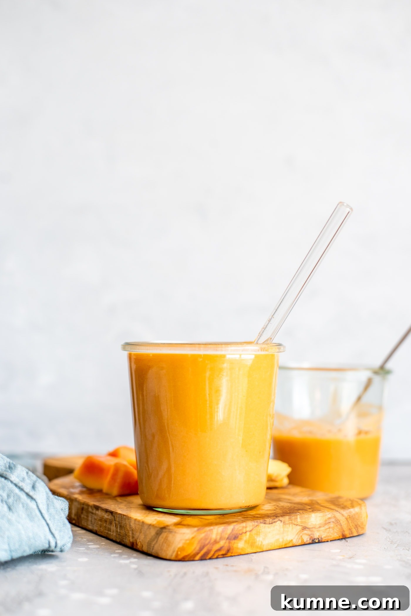 Vegan Papaya Smoothie in a glass on a cutting board with some chopped pieces of papaya and ginger.