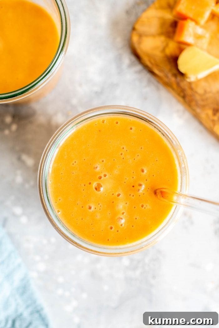Papaya carrot smoothie in a glass with a straw.