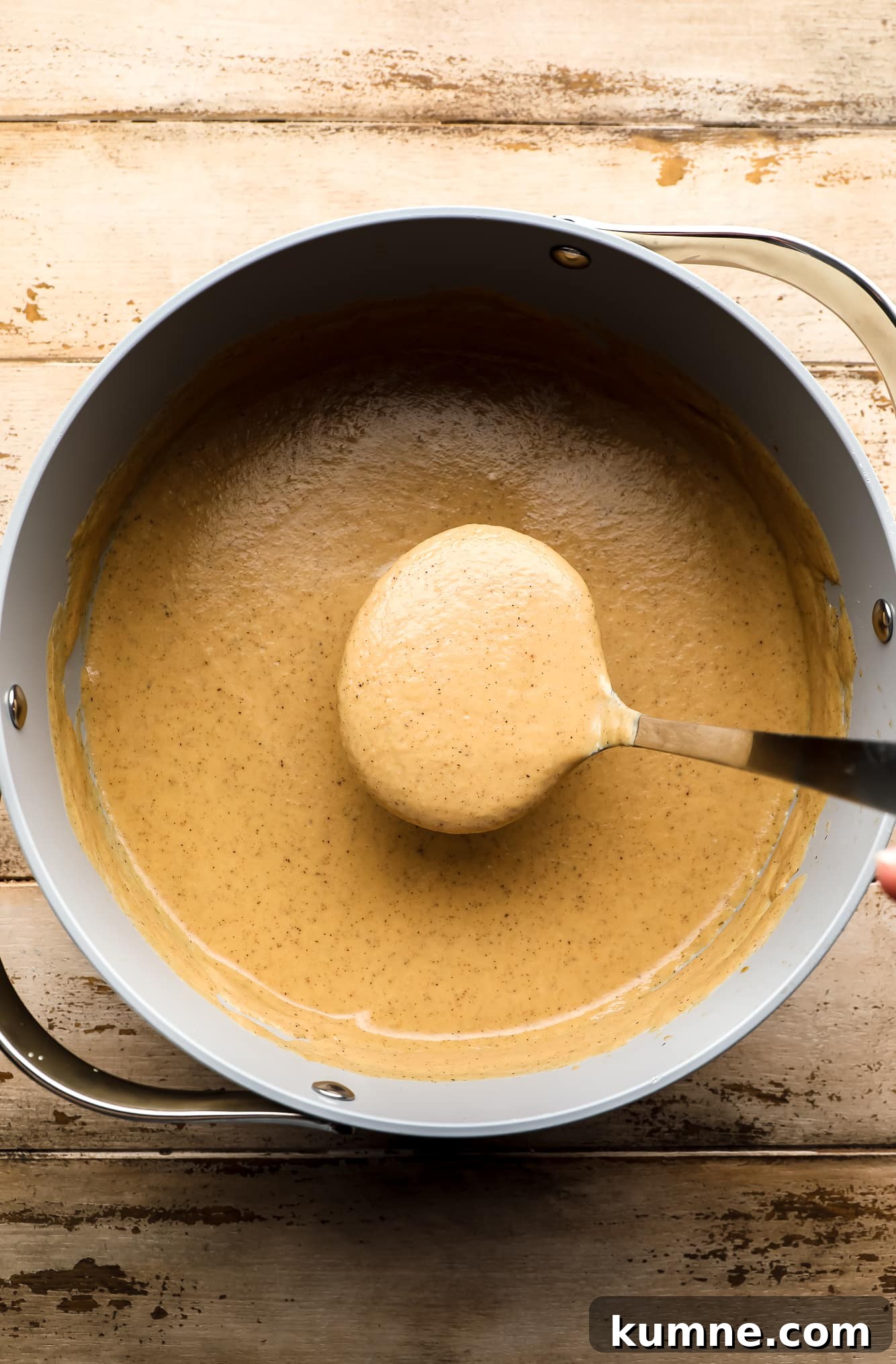 a ladle lifting a scoop of cauliflower soup from a large batch in a grey pot.