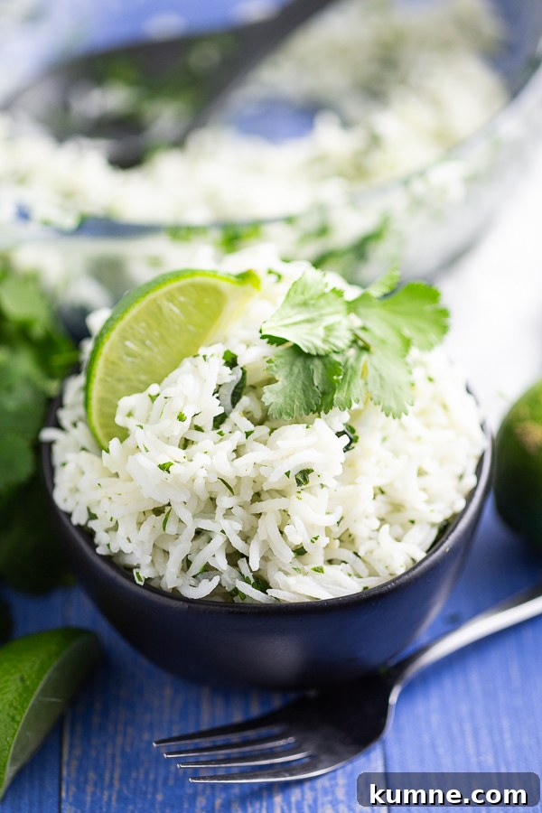 Chipotle-Style Cilantro Lime Rice Recipe for Flavorful Sides 2 White chipotle lime rice garnished with a fresh lime wedge and sprig of cilantro in a black bowl on a blue wood background
