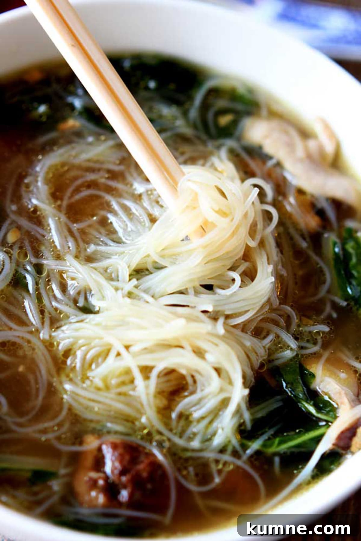Authentic Asian Chicken Noodle Soup Recipe for Comforting Flavor 3 White bowl of Asian Chicken Noodle Soup, rice noodles twirled on chopsticks.