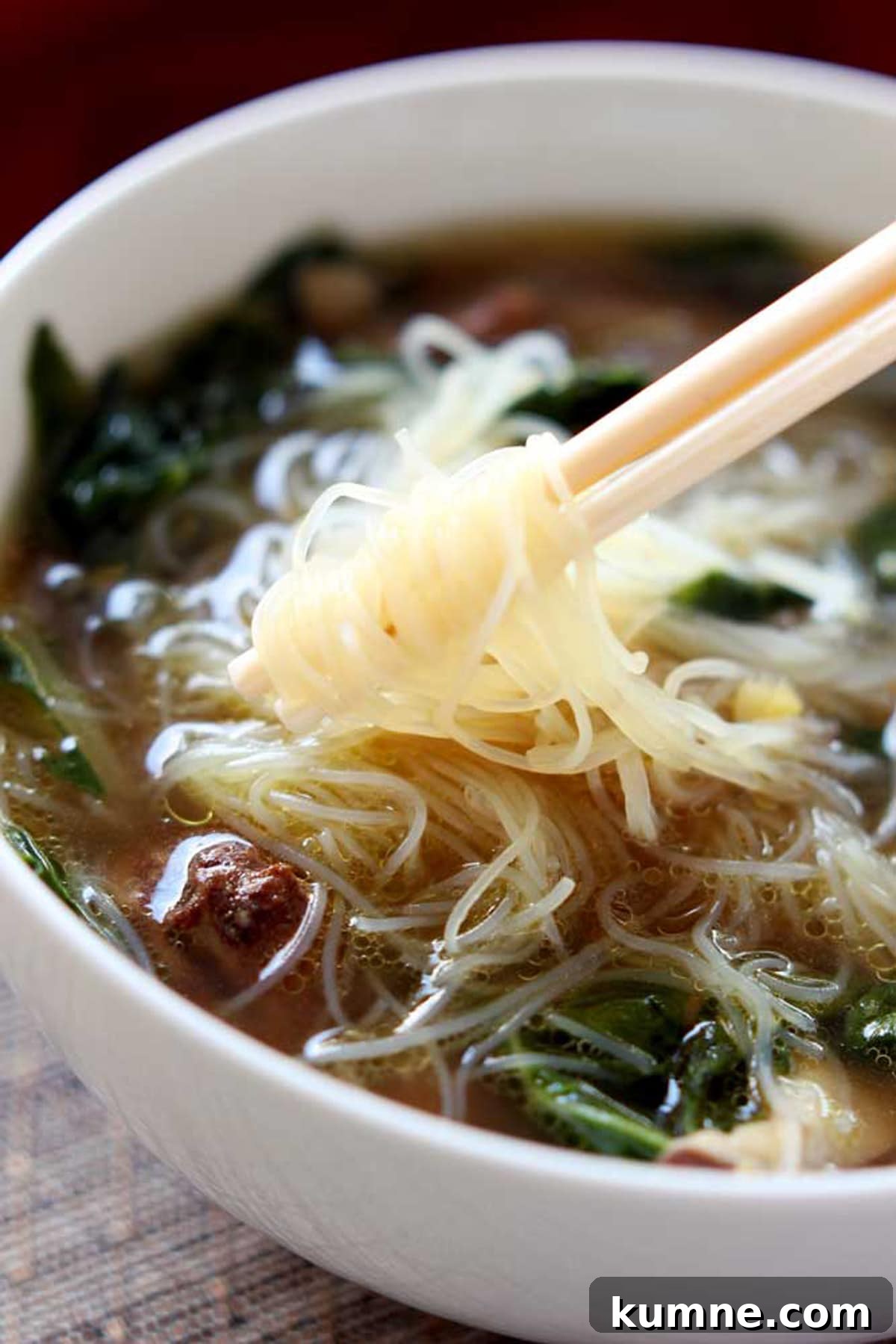 Authentic Asian Chicken Noodle Soup Recipe for Comforting Flavor 4 White bowl containing Asian Chicken Noodle soup, white chopsticks twirling Mei Fun noodles.