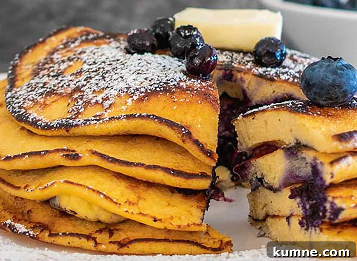 20+ Gluten-Free Blueberry Recipes for Delightful Desserts and Snacks 4 Coconut flour blueberry pancakes on a plate, topped with powdered sugar and cut open with a fork to reveal their fluffy, grain-free interior.