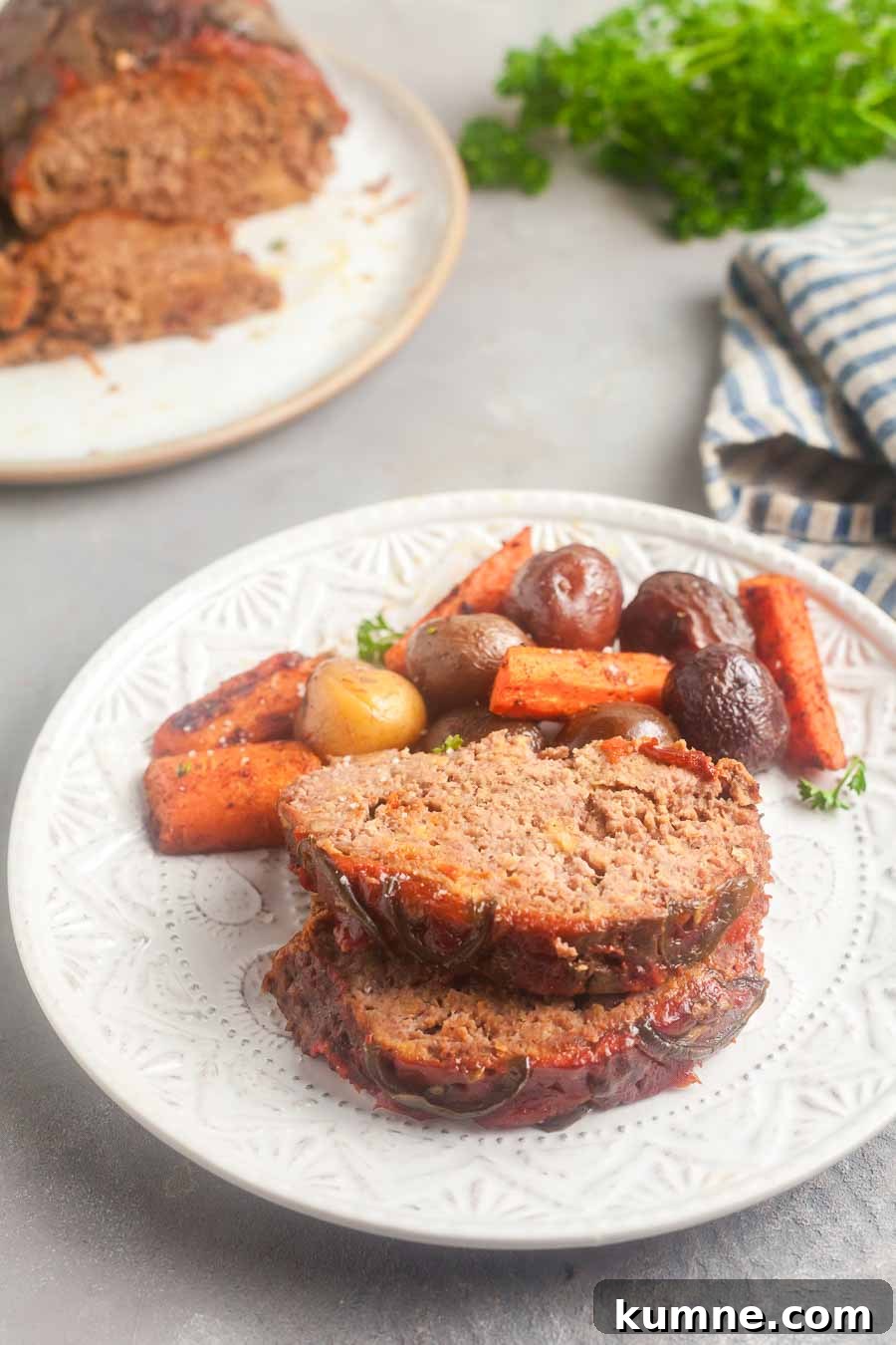 two slices of Thai barbecue meatloaf with potatoes and carrots on a white plate.