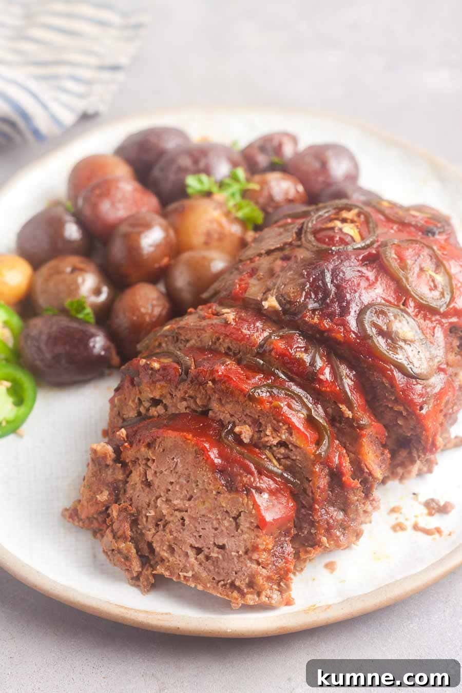 a partially sliced crockpot meatloaf on a serving plate, with potatoes in the background