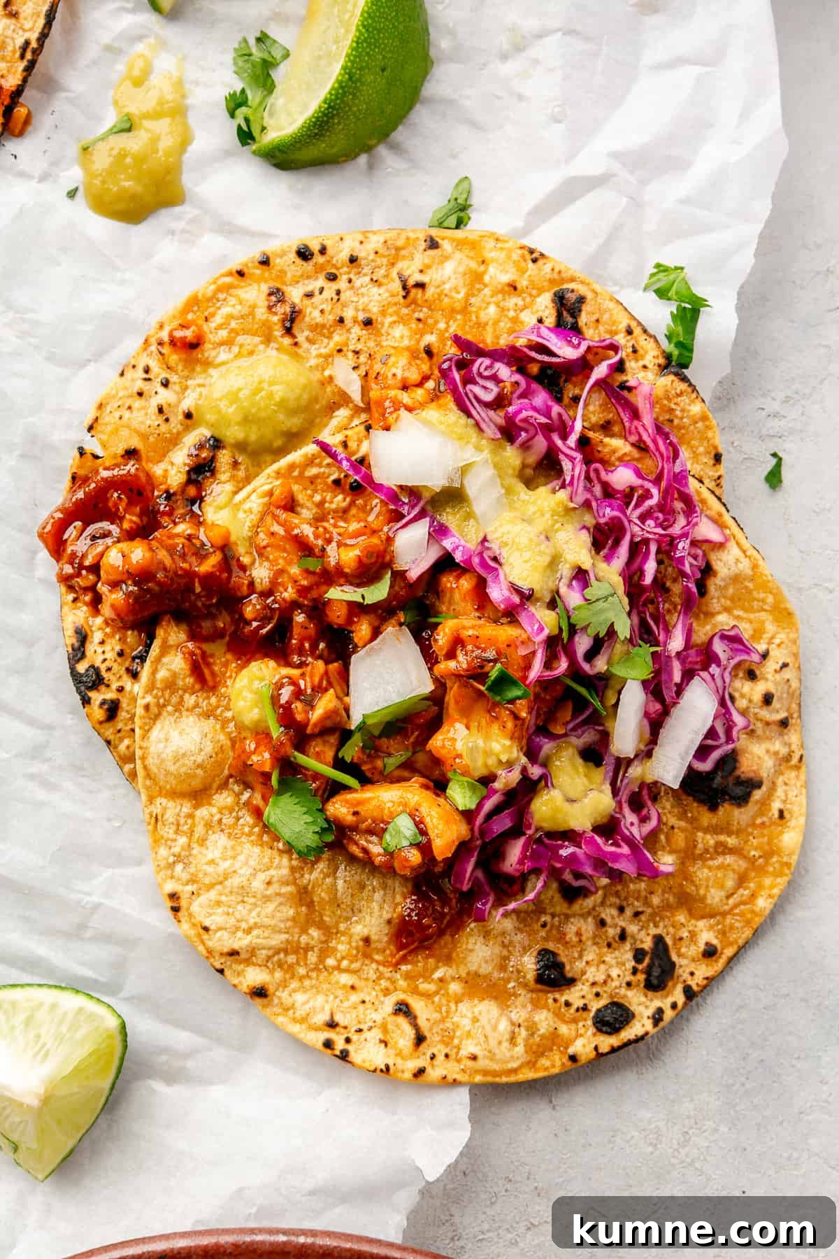 Sticky Chipotle Chicken Tacos with Smoky Lime Slaw 2 A Saucy Chipotle Chicken Taco on a piece of parchment paper. Lime wedges scattered around.