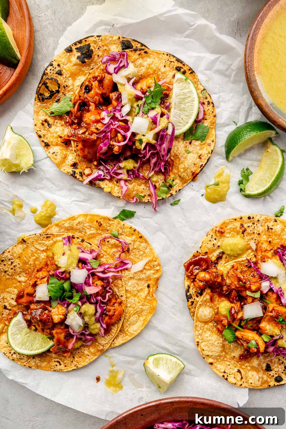 Sticky Chipotle Chicken Tacos with Smoky Lime Slaw 9 Three Saucy Chipotle Chicken Tacos on parchment paper. Lime wedges scattered around.