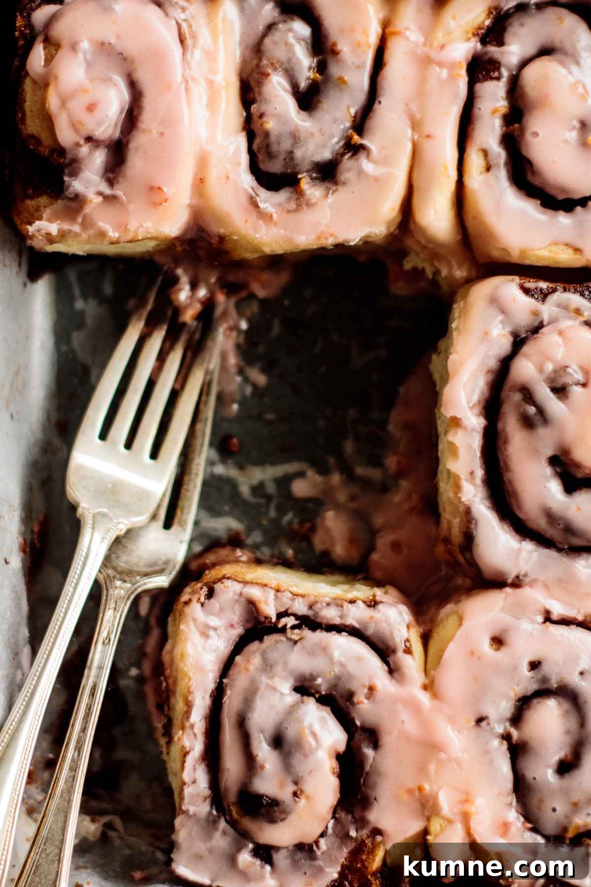 Pink Blood Orange Cinnamon Rolls with Zesty Glaze 6 Blood orange cinnamon rolls with pink glaze and two forks on a baking pan.