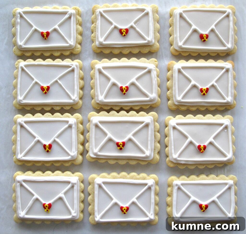 Valentine Sugar Cookies for Care Packages: Military Edition #9 2 Rows of 12 Valentine Envelope Sugar Cookies, rectangular sugar cookies with a scalloped edge iced white with white lines piped on top to look like the back of an envelope. At the tip of each envelope flap is a red heart sprinkle that has a yellow icing ribbon piped on it.