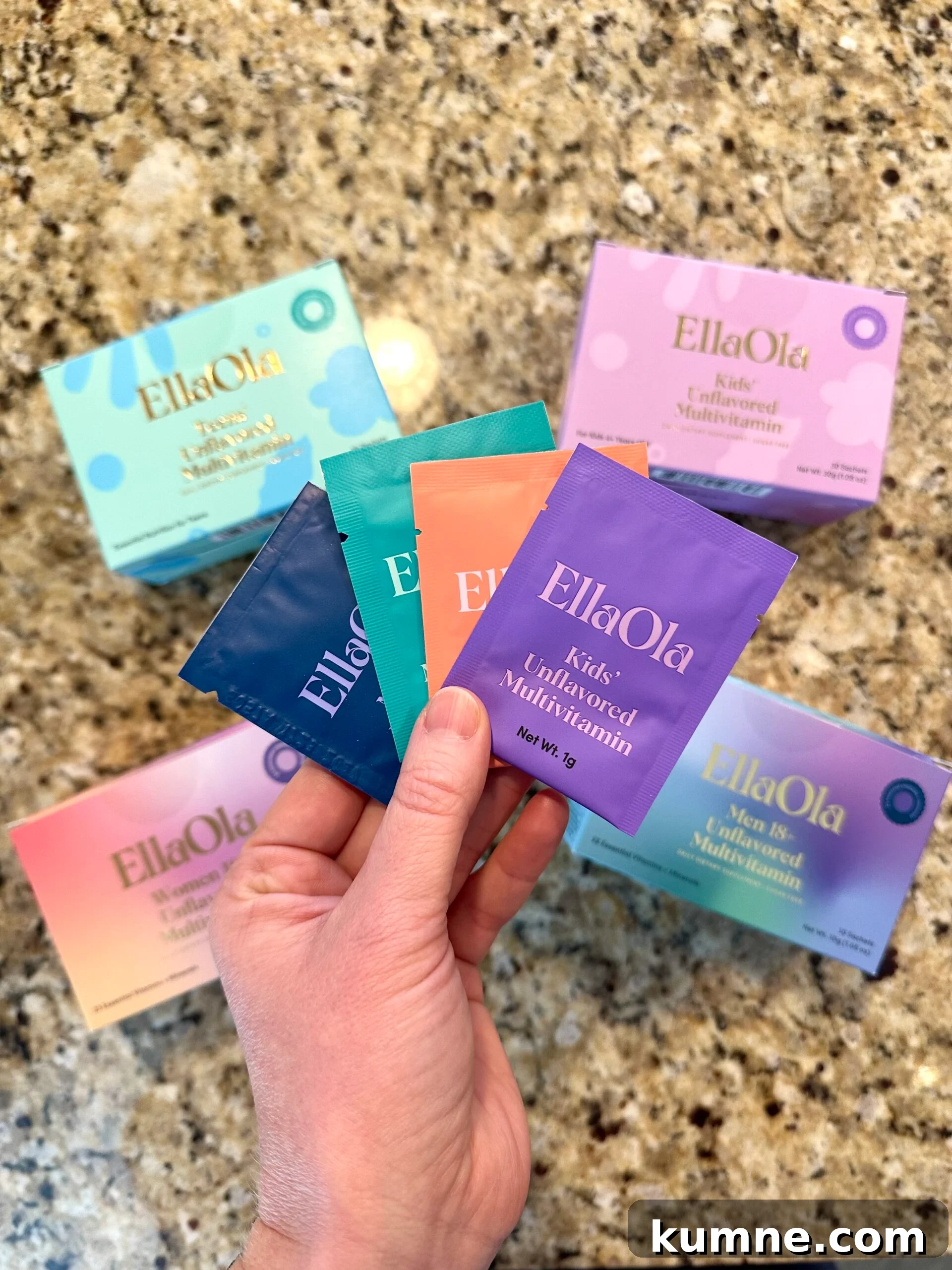 Organic Kids Vitamins: Top Picks Without Artificial Additives 2 Hand holding colorful EllaOla multivitamin packets, with various EllaOla supplement boxes spread out on a granite countertop.