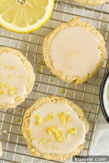 Almond flour lemon cookies topped with a glaze on a rectangular wire cooling rack with slices of lemon placed on the rack.