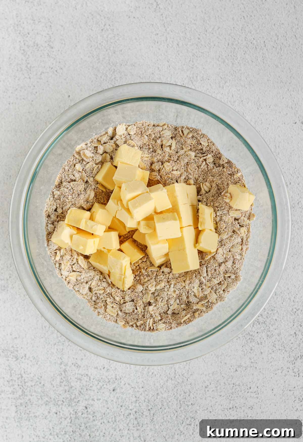 Whole Grain Low-Sugar Peach Crisp Recipe 6 Oats, oat flour, and coconut sugar mixed in a small glass mixing bowl with cubes of butter added to the bowl.