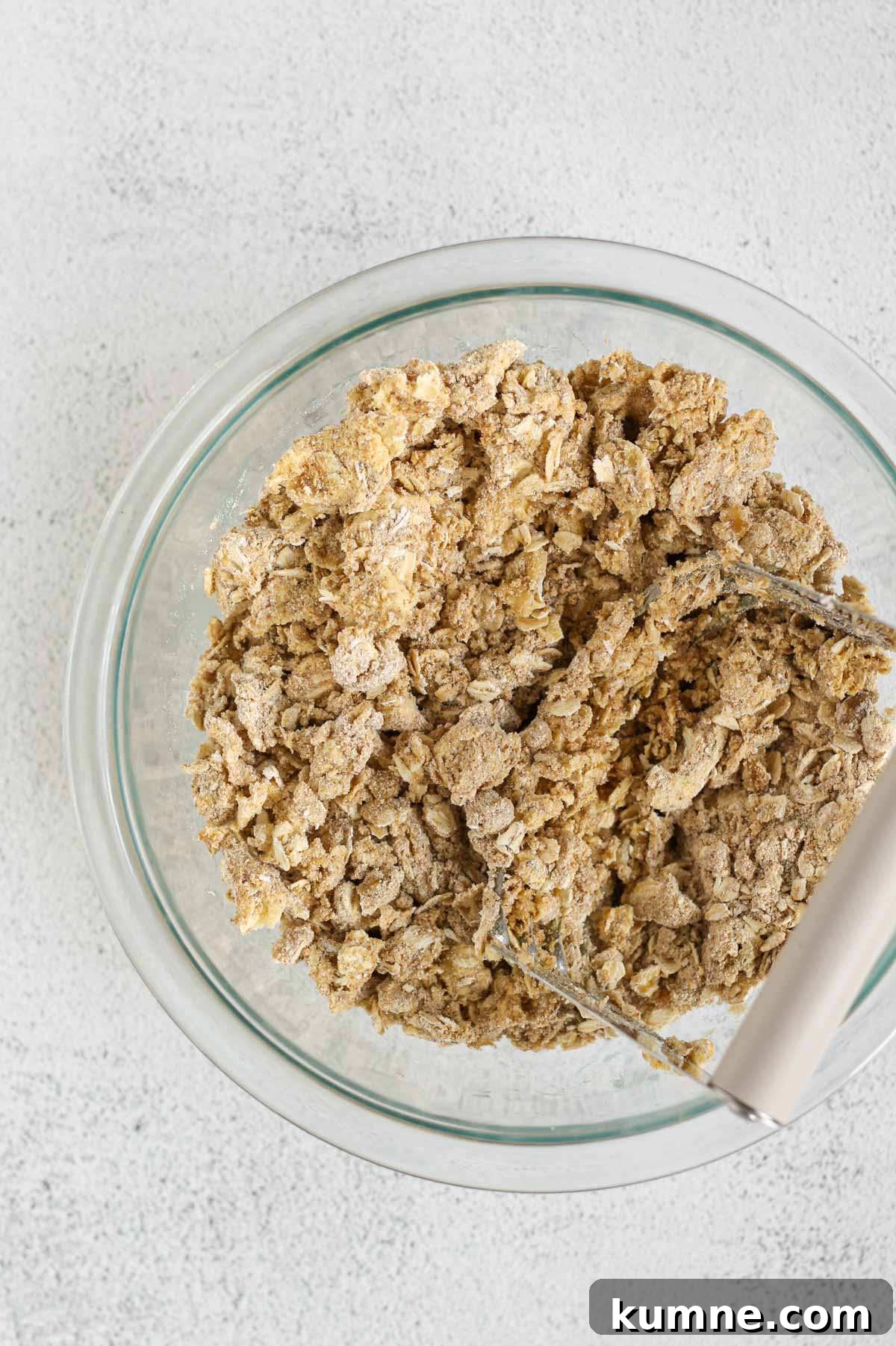 Whole Grain Low-Sugar Peach Crisp Recipe 7 Pastry cutter cutting butter into a mixture of oats, oat flour and coconut sugar in a small glass mixing bowl.