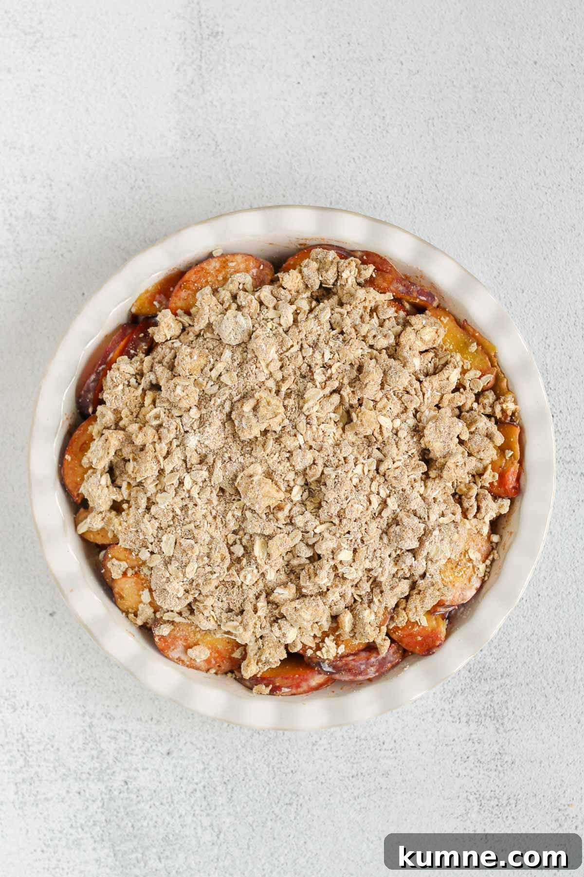 Whole Grain Low-Sugar Peach Crisp Recipe 8 Sliced peaches in a ceramic pie dish topped with oat flour, oat, and butter mixture.