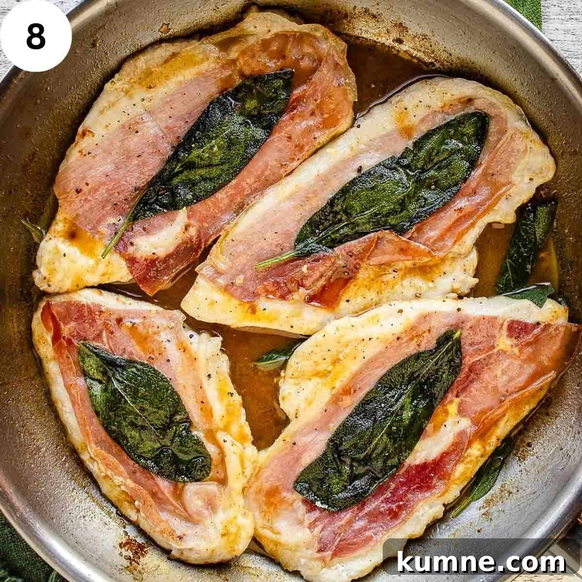 Four cooked chicken breasts each with prosciutto and a sage leaf in a pan.