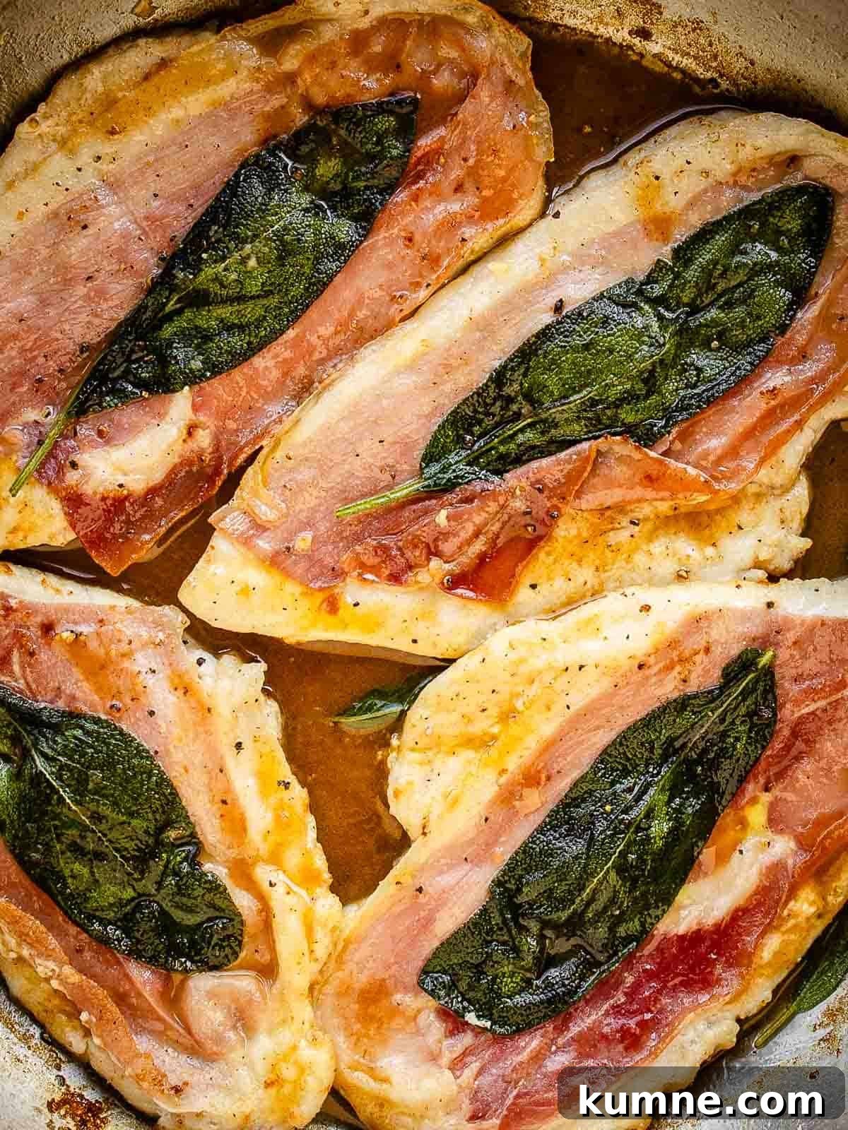 Four chicken cutlets with prosciutto and a sage leaf on each in a pan viewed from above.