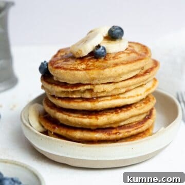 Stack of fluffy and healthy protein oatmeal blender pancakes topped with banana slices and blueberries.