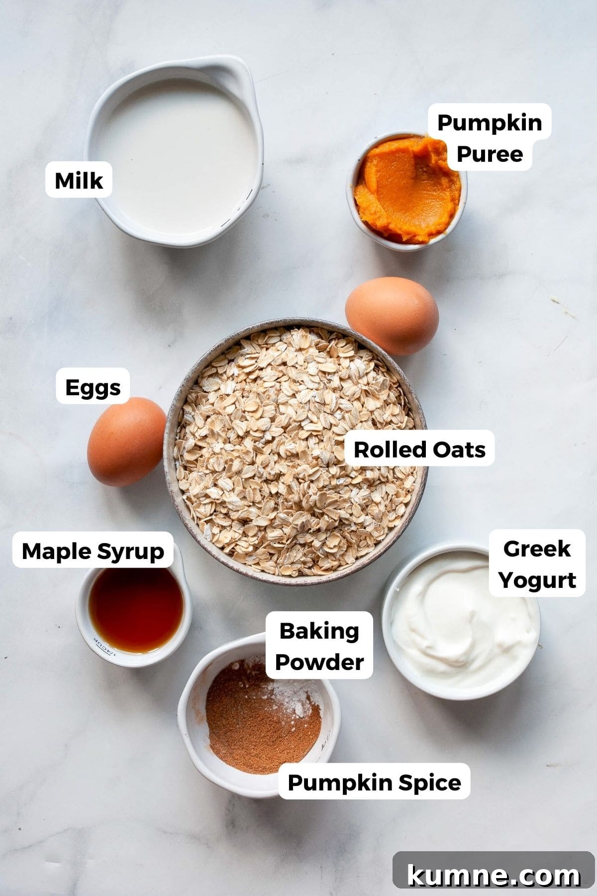 All pancake ingredients measured into small bowls with labels, including oats, pumpkin purée, Greek yogurt, eggs, maple syrup, baking powder, pumpkin spice, and salt.