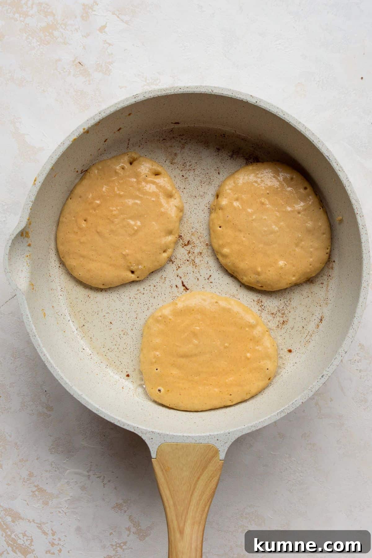 Three pumpkin protein pancakes cooking in a greased non-stick pan on the stove.