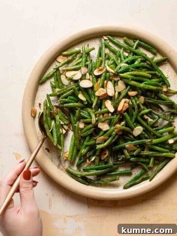 hand spooning from plate of green beans with almonds.