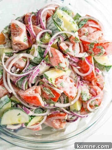 creamy cucumber tomato and onion salad in large glass bowl.
