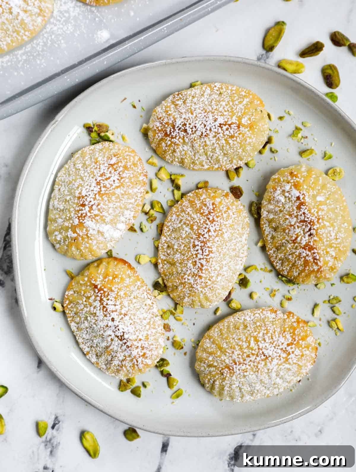 Pistachio Maamoul Cookies on a plate, dusted with sugar and garnished with pistachio chunks.