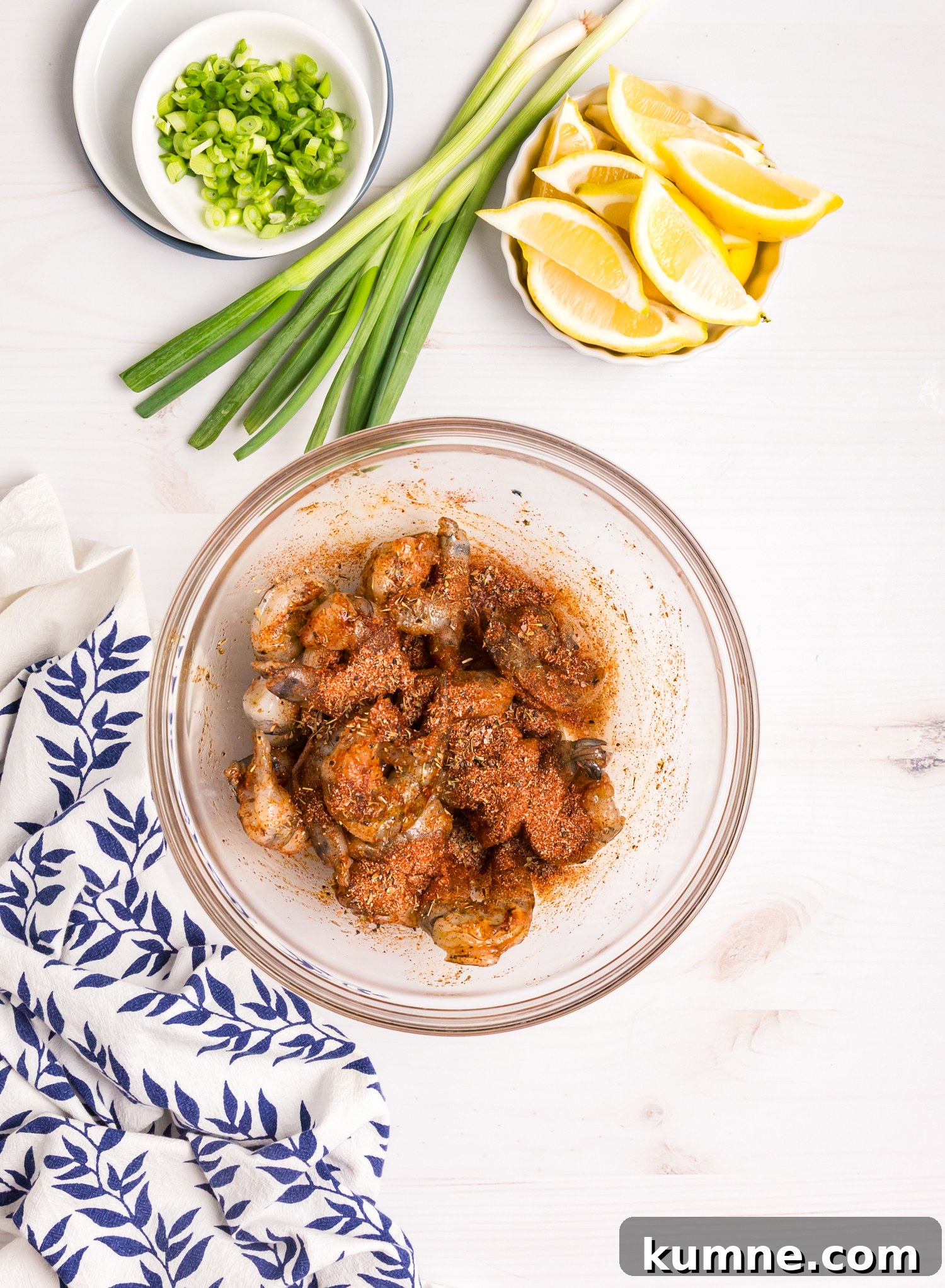 Seasoned raw shrimp in a bowl, coated evenly with spices, surrounded by fresh scallions and lemon slices.