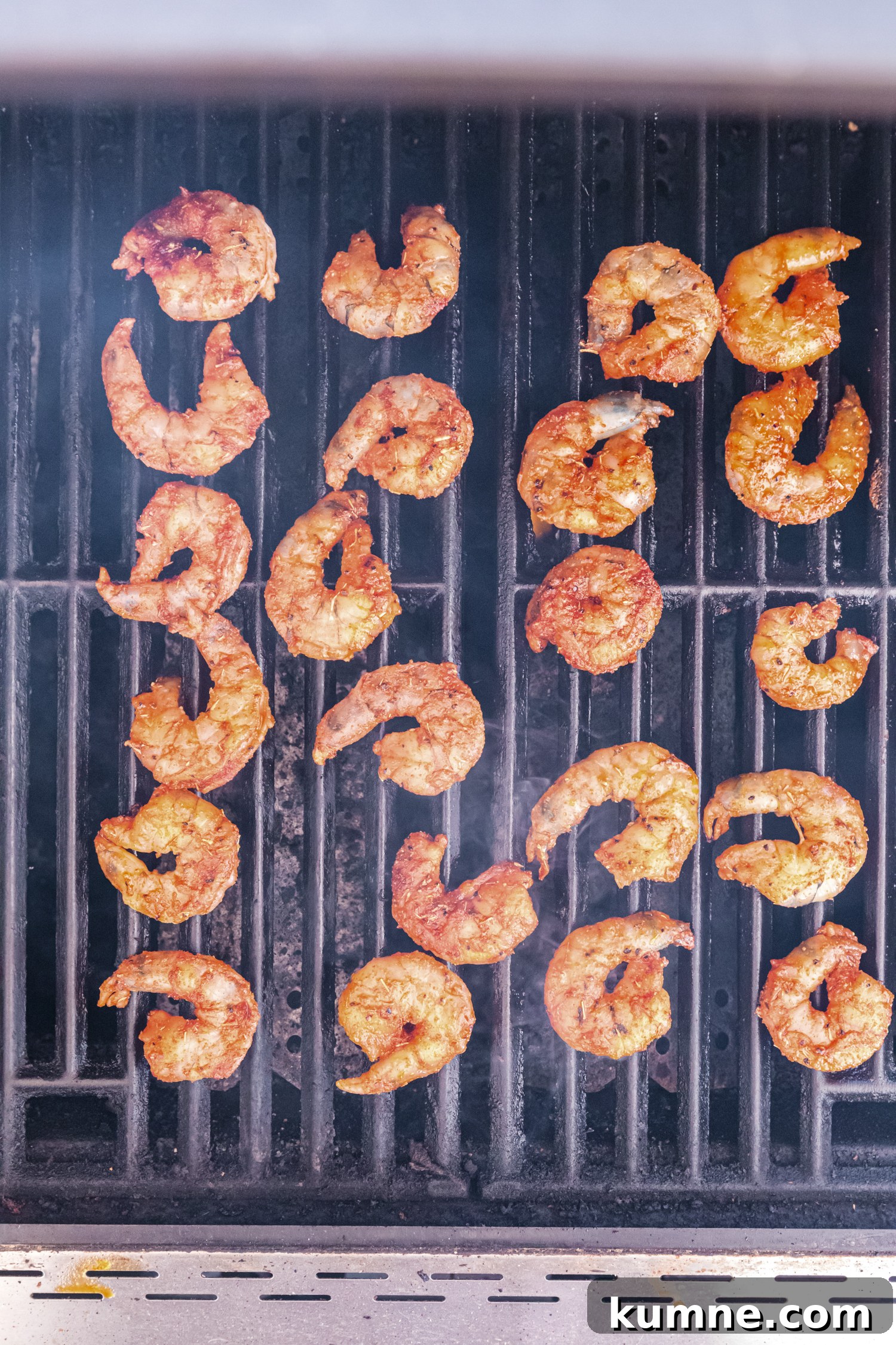 Spiced shrimp cooking on a grill, arranged in rows with visible grill marks.