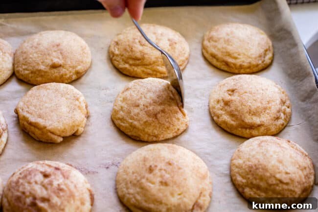 using a spoon to shape the edge of a cookie on a pan right after baking.