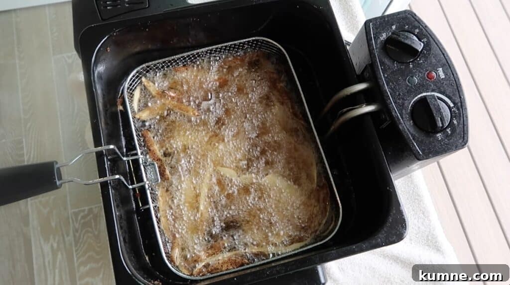 Potato sticks in basket submerged in oil
