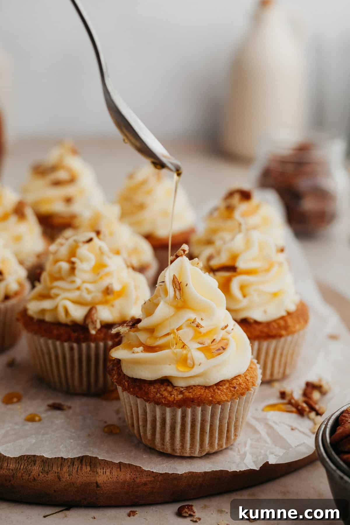 Maple Cupcakes Recipe with Brown Butter Frosting 9 cupcakes with white frosting, the cupcake at the front is being drizzled with maple syrup