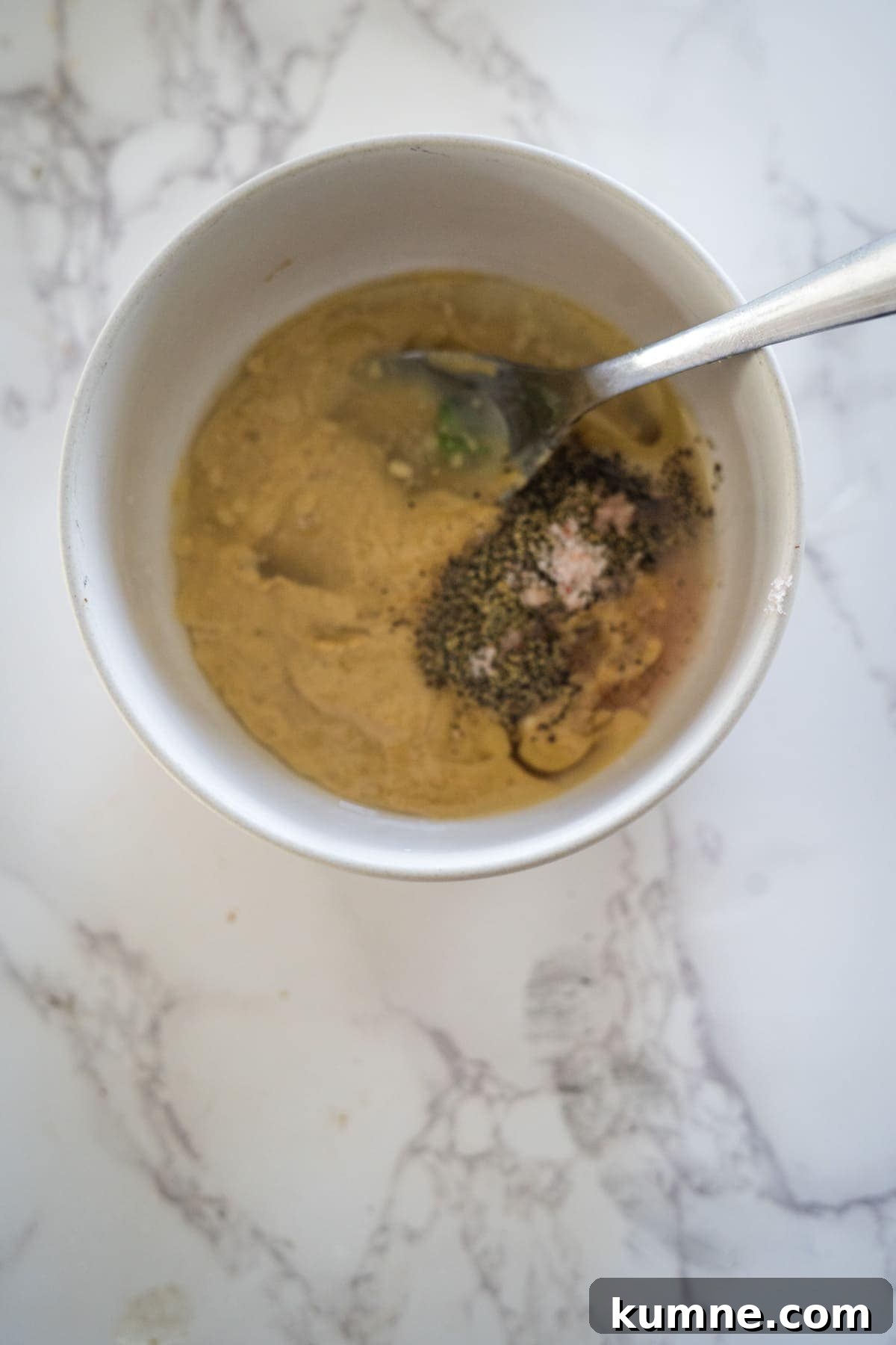 A bowl of soup with vegetables, tahini, and seasoning on a marbled surface.