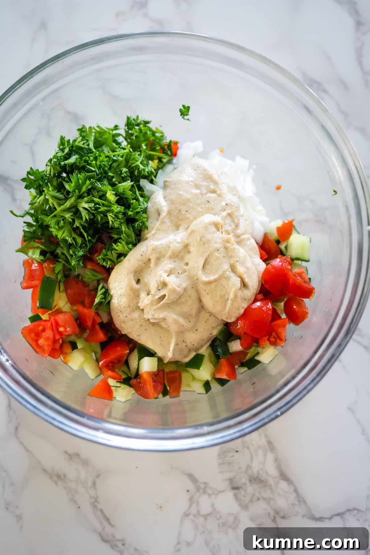 Fresh ingredients in a bowl, including diced tomatoes, cucumbers, onions, parsley, and a dollop of creamy tahini dressing.