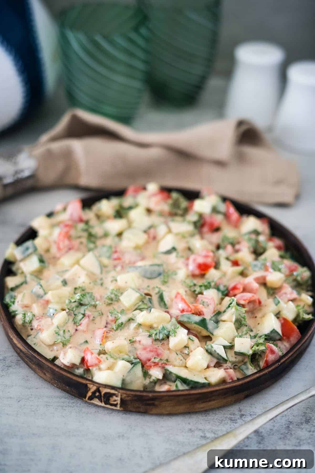 Fresh tahini vegetable salad on a wooden plate with a rustic table setting.