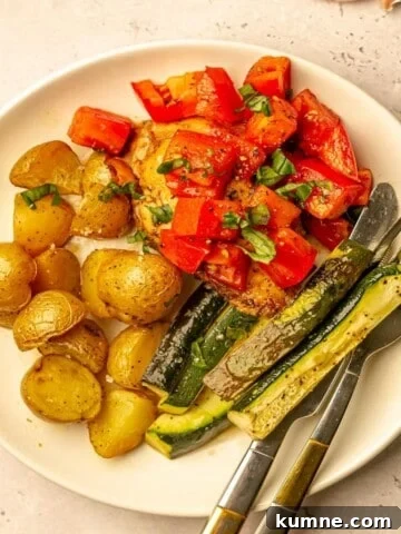 Chicken topped with tomatoes on a plate with zucchini and potatoes.