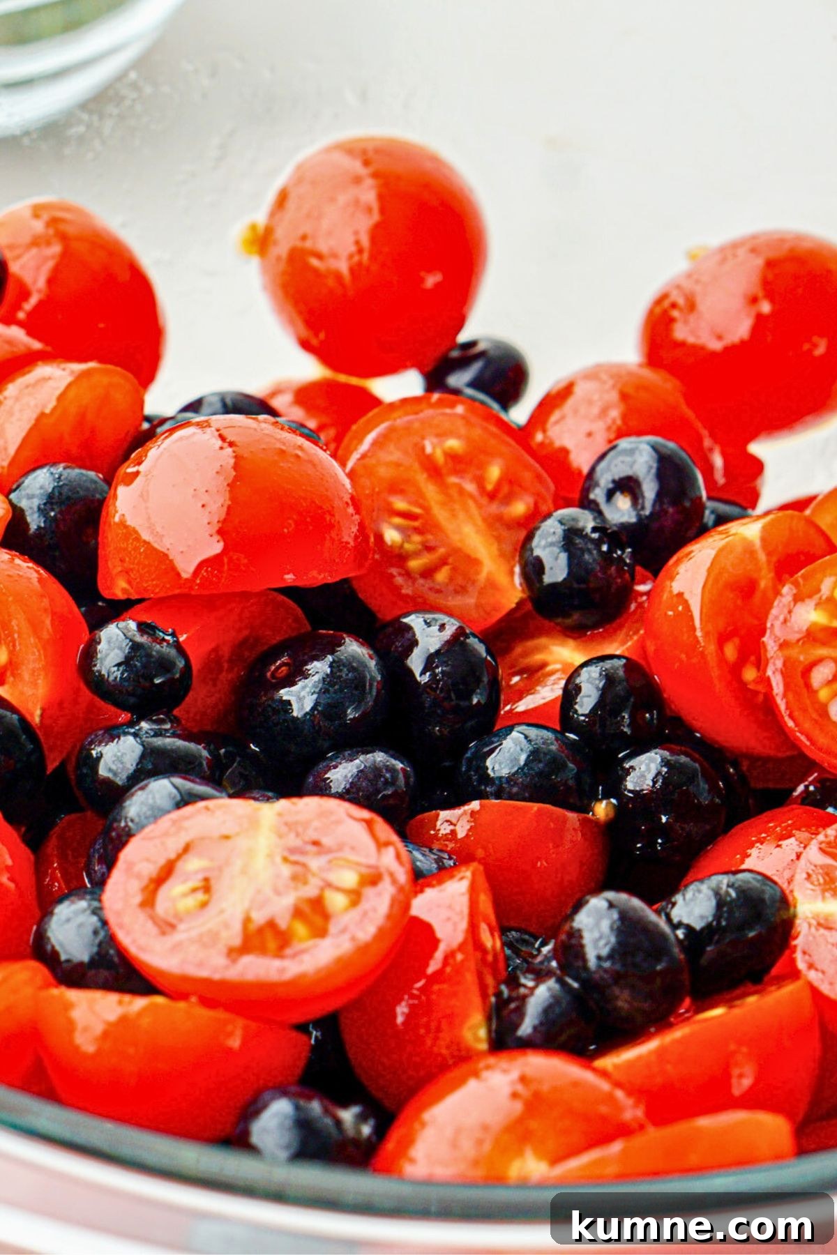 Berry Caprese Salad with Balsamic Glaze and Fresh Basil 5 Blueberries and cherry tomatoes in a clear glass bowl tossed with oil and balsamic vinegar.