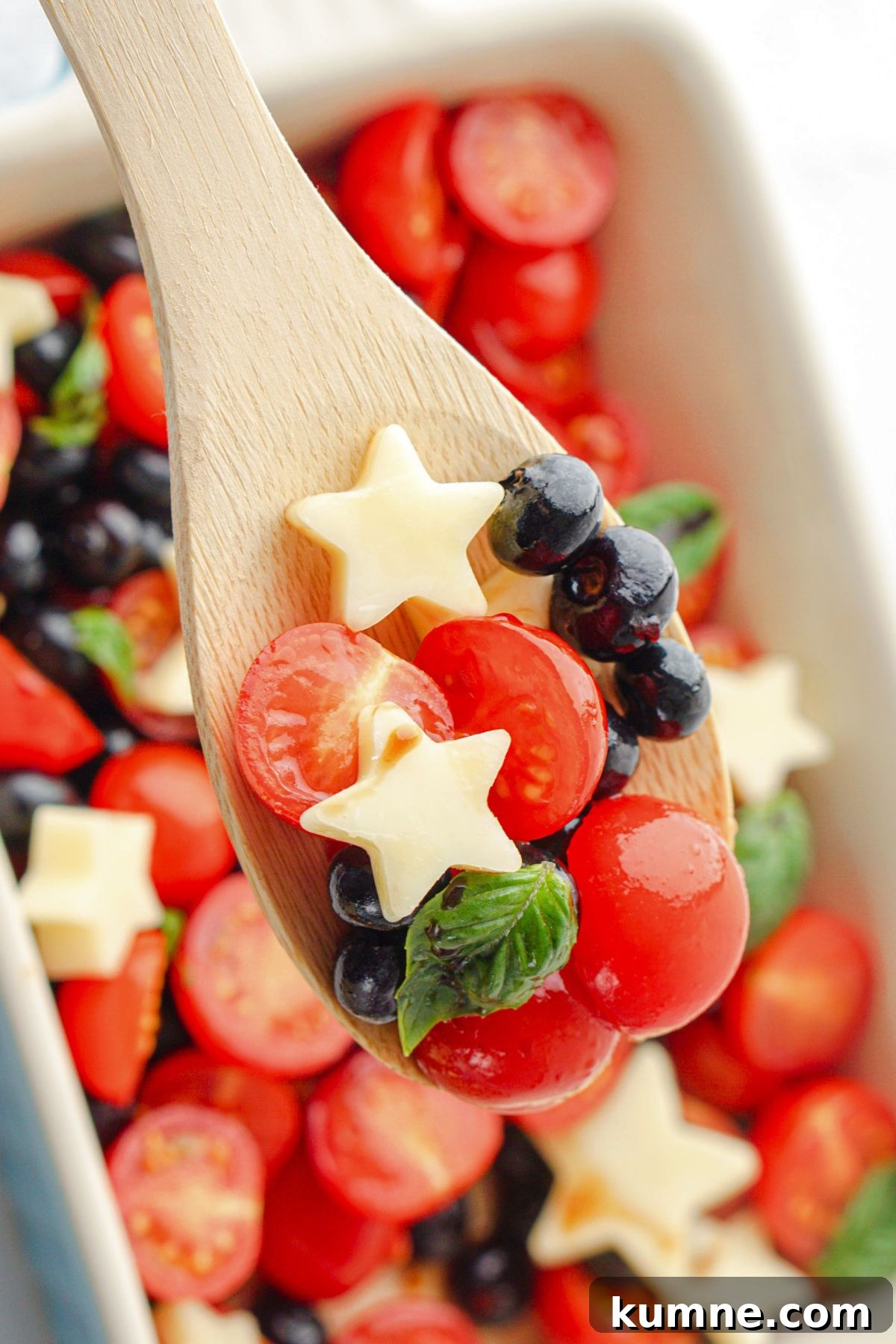 Berry Caprese Salad with Balsamic Glaze and Fresh Basil 8 Spoonful of berries, tomatoes, and stars on a wooden spoon.